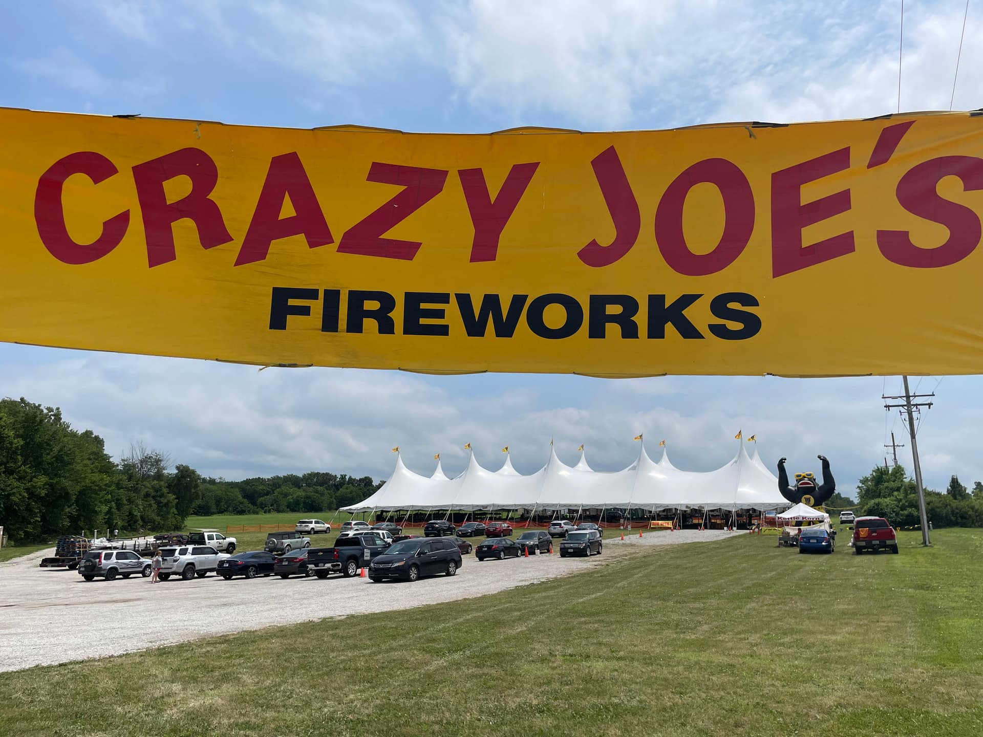 The huge yellow Crazy Joe's Fireworks overhead banner at the entrance to the stand at 171st & Holmes in Kansas City — the white event tents, the inflatable Joerilla mascot, and a parking lot full of customer cars are visible below